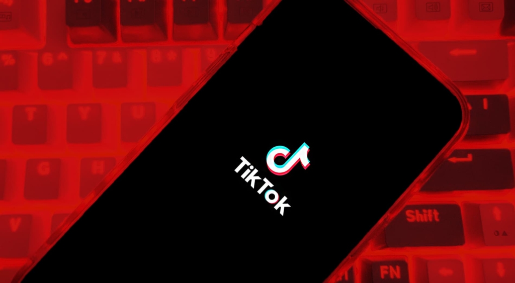 Tiktok logo on a mobile phone held over a keyboard with a red background